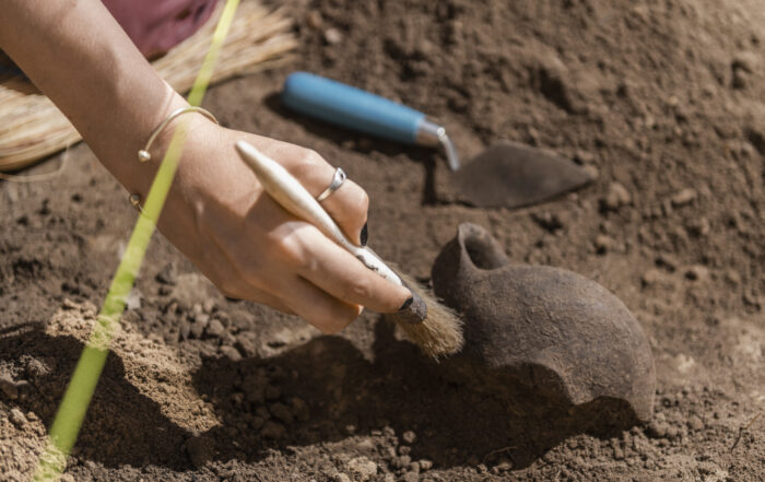 Female archaeologist digging up ancient pottery object at an archaeological site.